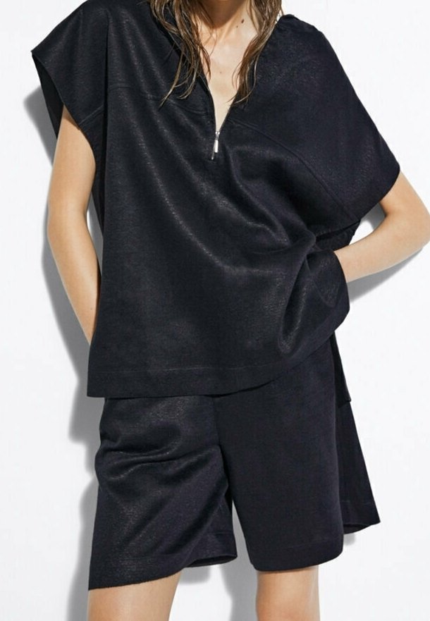 Svart tvådelad outfit med en kortärmad topp med kvartdragkedja och matchande shorts, tillverkad av ett slätt, texturerat tyg.