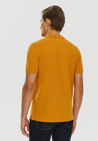 Koszulka polo z krótkim rękawem w pomarańczowym kolorze, wykonana z bawełny, z klasycznym kołnierzykiem, bocznymi rozcięciami u dołu i gładkim, teksturowanym wykończeniem.