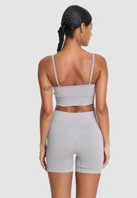 Szary sportowy zestaw składający się z topu krótko-kroju i szortów. Wykonany z elastycznej tkaniny, charakteryzuje się minimalną liczbą szwów i regulowanymi ramiączkami. Gładka struktura i dopasowany krój.