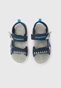Παιδικά σανδάλια KangaROOS σε μπλε και γκρι χρώμα με ρυθμιζόμενους ιμάντες και σχέδιο μ ε δόντια καρχαρία στους ιμάντες του ποδιού, σε λευκό φόντο.