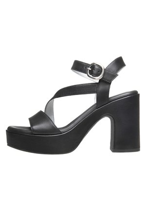 Black leather high-heeled sandals with a thick platform, crisscross straps, and a side buckle detail. Smooth texture and minimalist design.
