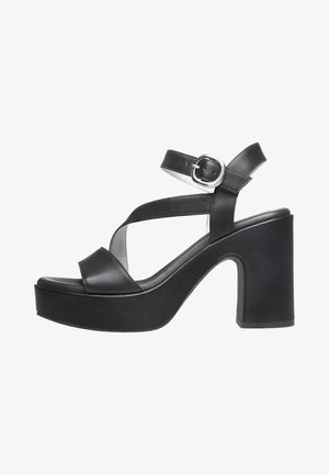 Black leather high-heeled sandals with a thick platform, crisscross straps, and a side buckle detail. Smooth texture and minimalist design.