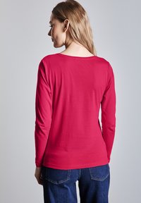 Długie rękawy w intensywnym różowym kolorze z bawełny, z okrągłym dekoltem i dopasowanym krojem, zestawione z ciemnoniebieskimi dżinsami.