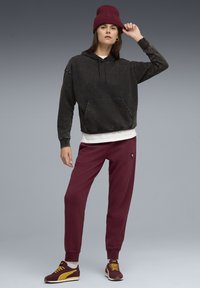 Sort, oversized hættetrøje med en frontlomme, hvid skjorte under, maroon sweatpants og burgunder strikket hue. Mørke sneakers med gule accenter.