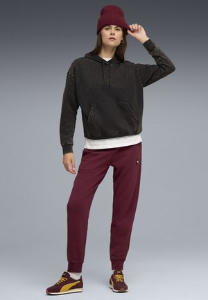 Black, oversized hoodie with a front pocket, white shirt underneath, maroon sweatpants, and burgundy knit beanie. Dark sneakers with yellow accents.