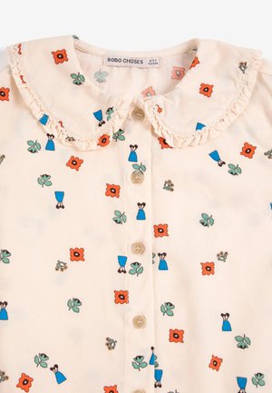 Chemisier enfant couleur crème avec col claudine volanté, motifs de fleurs orange et robe bleue, et boutons sur le devant. L'étiquette indique la taille 6-7 ans.