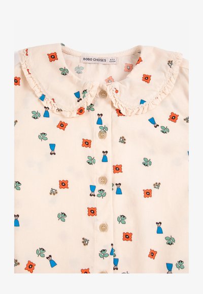 Chemisier enfant couleur crème avec col claudine volanté, motifs de fleurs orange et robe bleue, et boutons sur le devant. L'étiquette indique la taille 6-7 ans.