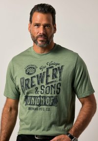 Camiseta de manga corta verde hecha de tela suave, con un gráfico de cervecería vintage en impresión oscura, cuello redondo y corte relajado.