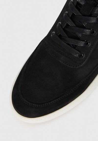 Must mustest sneakers, mille ümara toe, musta paeltega disain, ja valge kummist tallaga; sile tekstuur kontrastsete õmbluskestega.