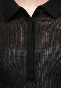 Μαύρο πλεκτό πόλο με ραβδώσεις, ημιδιάφανα κάθετα ριγέ και κουμπωτή λωρίδα στο λαιμό.