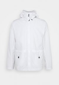 Chaqueta blanca con capucha, que presenta un cierre frontal, dos grandes bolsillos y detalles con cordones. Textura suave con detalles de diseño mínimos.