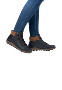 Bottines en cuir noir avec des accents marron, surface texturée, fermeture à lacets et à glissière, et une semelle en caoutchouc robuste pour une meilleure traction.