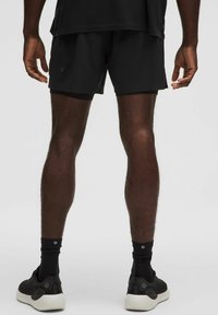 Shorts atletici neri con una texture liscia, abbinati a calzini neri alla caviglia e sneaker nere. I dettagli notevoli includono un design a strati.
