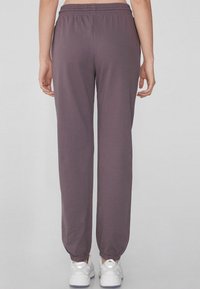 Joggers morados de tela suave con cinturilla elástica, puños ajustados y un ajuste relajado, combinados con zapatillas deportivas blancas.