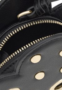 Czarna skórzana torba o teksturowanej powierzchni, wyposażona w złoty zamek błyskawiczny i złote akcenty. Wnętrze wyłożone ciemną podszewką, co tworzy kontrast.