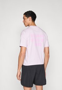 Hele-roosa lühikeste varrukatega t-särk, mille taga on graafiline trükk tekstiga „Running State of Mind“. Sobitatud mustade lühikestega.