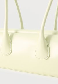 Χειροποίητη τσάντα από χρώμα απαλό κίτρινο δέρμα, με λεπτές λαβές και εμφανή ραφές, σε απλό ανοιχτό φόντο.