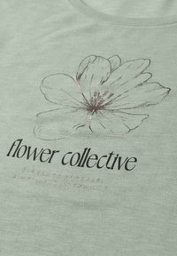 Grand croquis délicat de fleur au-dessus du texte « flower collective » sur un tissu vert clair, ressemblant à un design de t-shirt décontracté.
