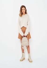 Ljust beige tröja, brun plisserad kjol och mönstrad ryggsäck. Klumpiga beige snörstövlar. Enkelt mönster, mjuka material och neutrala färger.