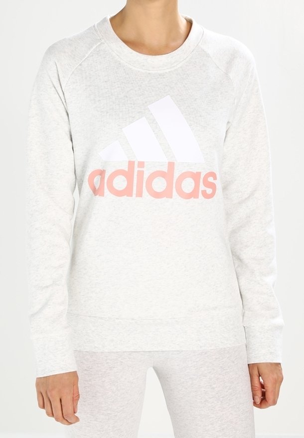 Persona che indossa un felpa Adidas grigia chiara con un grande logo bianco e rosa pallido sul petto.