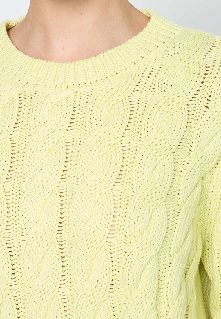 Pull en maille jaune clair avec un motif en câble, col rond et bords côtelés. La texture semble douce et épaisse.