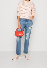 Světle růžová mikina s puntíky, roztrhané modré džíny, červená mini kabelka a světle sportovní boty s akcenty růžové a žluté.