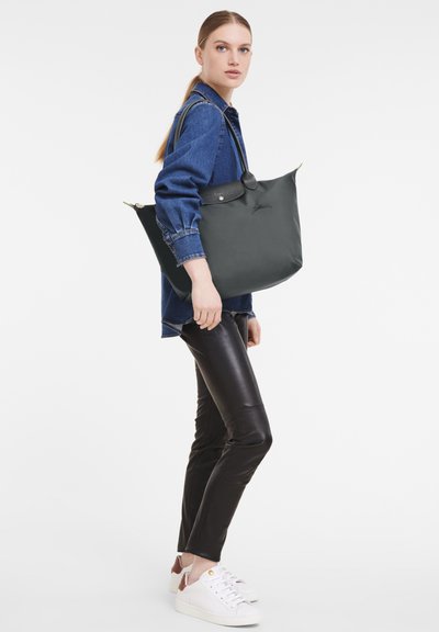 Black tote bag made of smooth material with a structured shape, featuring a top closure and contrasting handles. Minimalistic design.