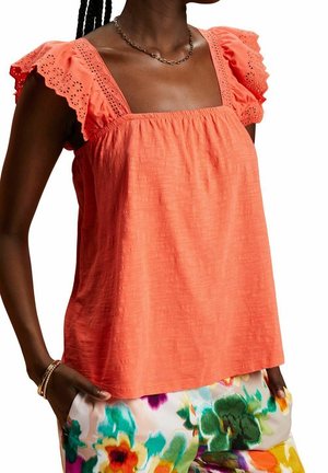 Blouse corail à encolure carrée, manches à volants bordées de dentelle et tissu texturé ; associée à un pantalon à motif floral.