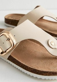 Beige sandalen met een brede band, een gouden gesp en een bruine kurken voetbed. De witte gestructureerde zool biedt contrast en grip.