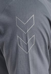 Grijze sportshirt met een soepele textuur, voorzien van drie naar boven wijzende chevrons in het wit op de bovenrug.