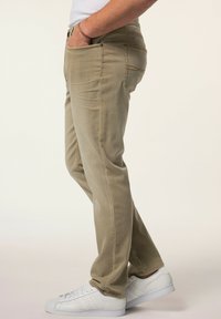 Pantalones de mezcla de algodón beige con piernas rectas, bolsillos frontales y costuras en contraste. Combinados con zapatillas blancas para un look casual.
