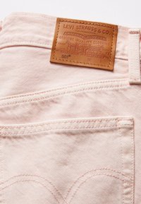 Jeans de mezclilla rosa claro con una etiqueta de cuero que presenta "Levi Strauss & Co." y "501". Costura notable y diseño tradicional de bolsillos.
