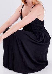 Robe maxi noire avec bretelles spaghetti réglables, corsage texturé et jupe fluide. Tissu doux et léger qui tombe jusqu'au sol.