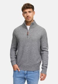Grå ulltröja med halv dragkedja, ribbade ärmslut och nederkant, med ett läderdetalj vid sidan. Stylar med blå jeans.