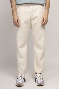 Pantalons en coton beige clair avec une coupe droite, des coutures visibles et une texture subtile. Associés à des baskets grises et blanches.