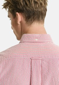 Rot-weiß gestreiftes Shirt mit einem Button-Down-Kragen, Rückenteil und einem einzelnen Knopfdetail am Kragen. Weicher Stofftextur.