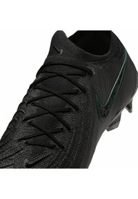 Schwarzer Fußballschuh aus strukturiertem Material, mit schwarzen Schnürsenkeln und einem grünen Akzentstreifen an der Seite. Schlankes, kantiges Design.