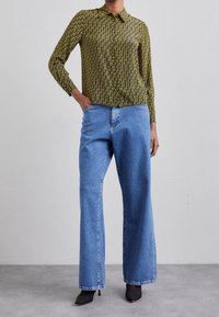 Camicia a maniche lunghe con colletto di colore giallo, decorata con un motivo geometrico nero, abbinata a jeans in denim blu a vita alta e gamba larga, con tacchi neri.