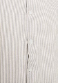 Gros plan d’un tissu beige et blanc à rayures verticales avec trois boutons blancs cousus le long de la couture centrale d’une chemise.