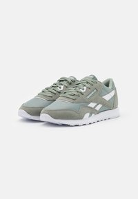 Par de zapatillas Reebok Classic en gris-verde con franjas blancas, detalles de ante y suelas de goma blanca sobre un fondo blanco.