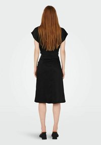 Abito nero a linea ad A con maniche corte e vita; tessuto morbido; lunghezza al ginocchio; abbinato a scarpe con tacco a blocco.