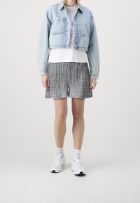 Veste en denim courte, bleu clair, avec deux poches avant. T-shirt blanc en dessous. Shorts à carreaux noir et blanc. Baskets blanches.