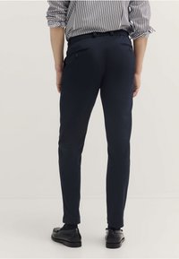 Granatowe spodnie o dopasowanym kroju, z tylnymi kieszeniami i gładką teksturą. W zestawie z czarnymi butami i koszulą w paski.