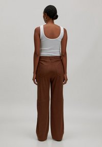 Weißes Tanktop mit Rundrücken, kombiniert mit braunen weiten Hosen mit Gesäßtaschen und glatter Textur.