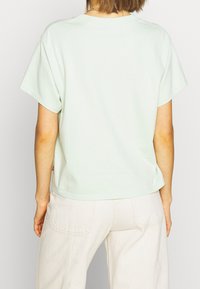 Mátově zelené tričko s krátkým rukávem, kulatým výstřihem, volným střihem a bočními rozparky. Tkanina vypadá měkká a lehká.