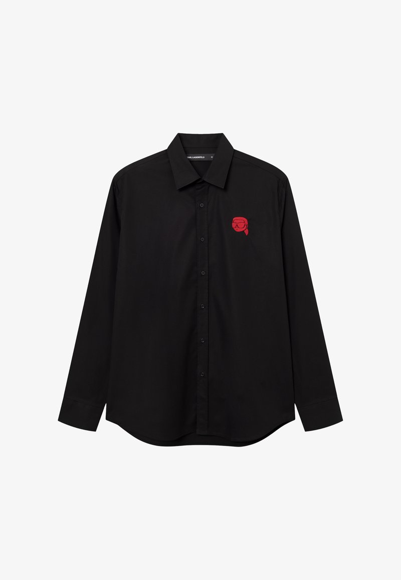 Chemise noire à manches longues avec boutons, col pointu et petit motif rouge représentant une tête portant des lunettes de protection sur le côté gauche de la poitrine.