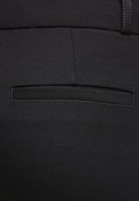 Svart tygficka på byxor, med en elegant design och en slät textur. Fickan är prydligt sydd i plagget.