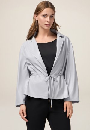 Jasnoszara, zapinana kurtka z szerokimi rękawami i kołnierzem, wykonana z gładkiego materiału; noszona na czarnej bluzce. Prosty, nowoczesny design.