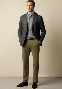 Męski strój z brązową kraciastą marynarką, szarym dzianinowym polo, oliwkowymi spodniami i ciemnobrązowymi loafersami, o gładkiej strukturze.