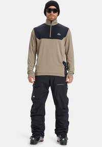 Beige og marineblå lynlåset langermet top kombineret med sorte cargo bukser. Toppen har et logo og tekstureret stof; bukserne har flere lommer.